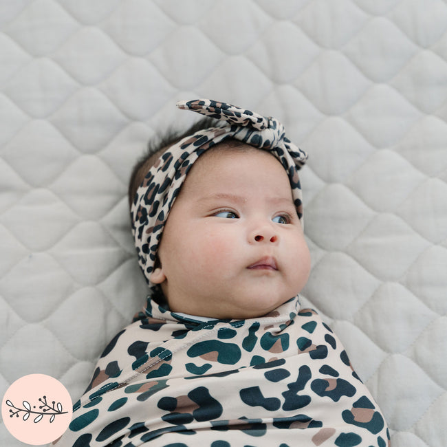 Close up of baby swaddled in brown leopard print baby swaddle and headband