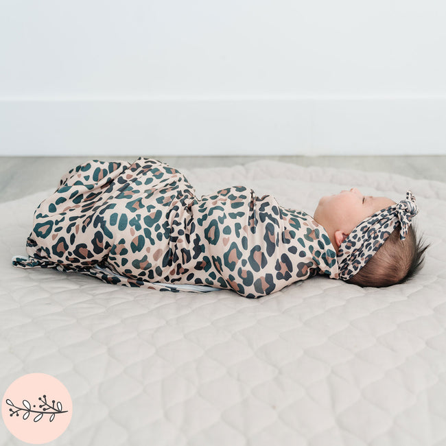 Newborn baby girl swaddled in brown leopard print baby swaddle and headband