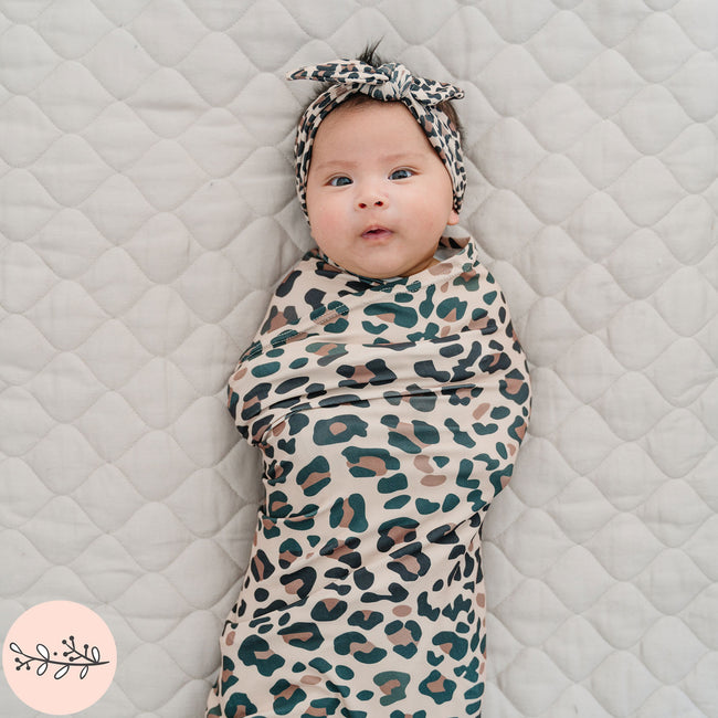 A baby swaddle blanket with brown leopard print design with a matching headband