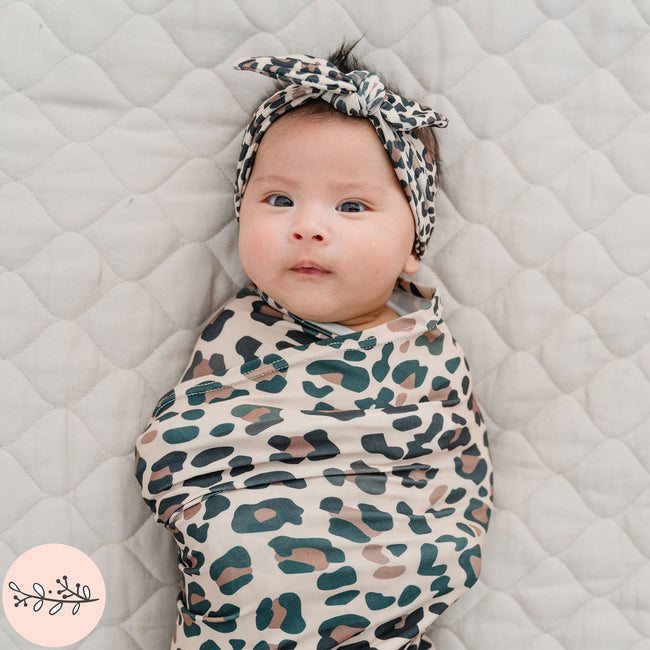 Close up of baby swaddled in brown leopard print baby swaddle and headband