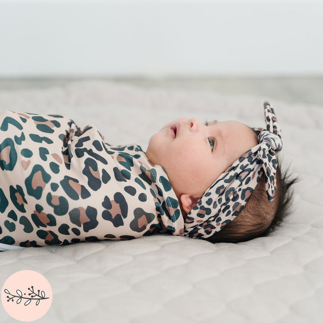 Close up of baby swaddled in brown leopard print baby swaddle and headband