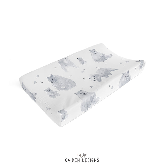 A baby changing pad cover featuring a watercolor-style print of polar bears and small geometric shapes on a white background, styled on a neutral surface.