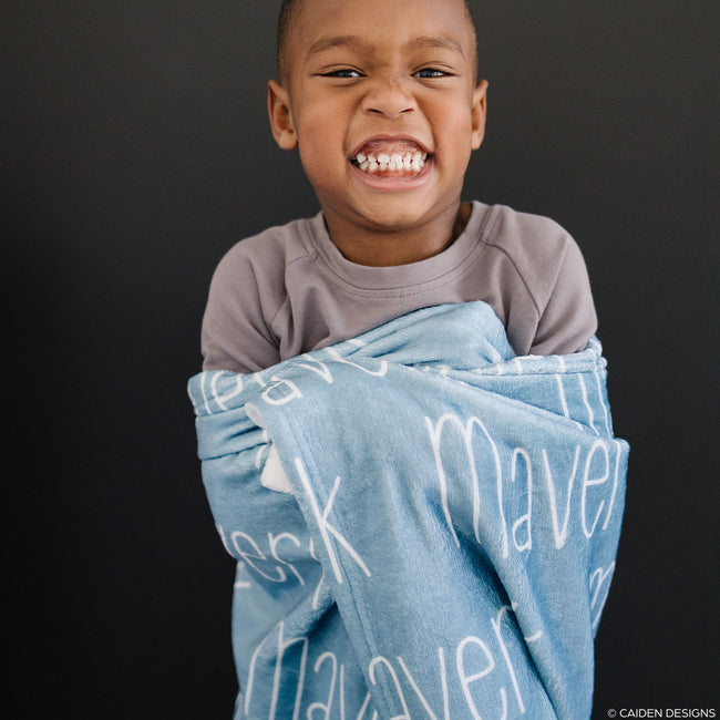 A young boy with a blue personalized blanket with the name 'Maverick' printed in a white font.
