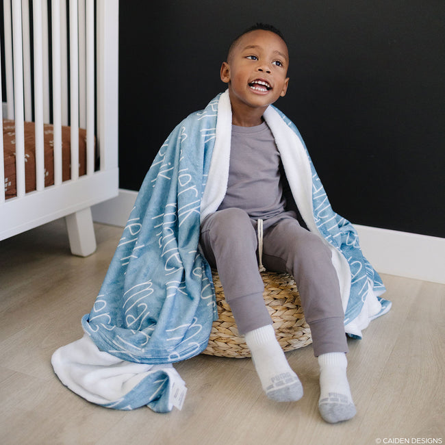 A young boy with a blue personalized blanket with the name 'Maverick' printed in a white font.