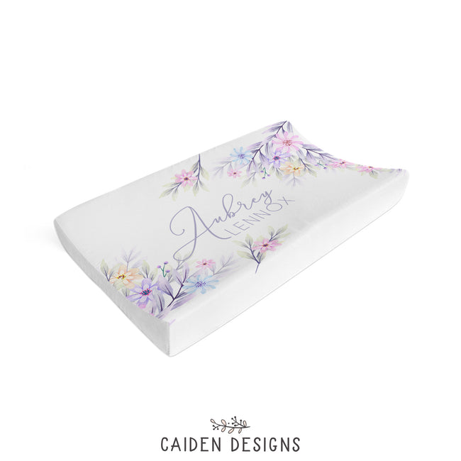 A personalized changing pad cover with a pastel watercolor flowers design and custom text.