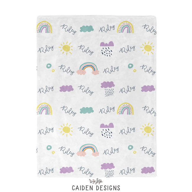 A personalized blanket with a rainbows, clouds, and suns pattern and the name 'Riley' printed repeatedly.