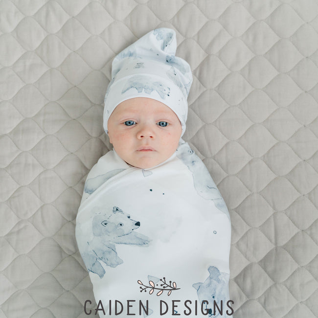 A baby wrapped in a monochrome watercolor polar bear swaddle blanket with a matching baby hat