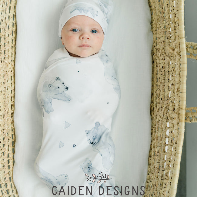 A baby wrapped in a monochrome watercolor polar bear swaddle blanket with a matching baby hat