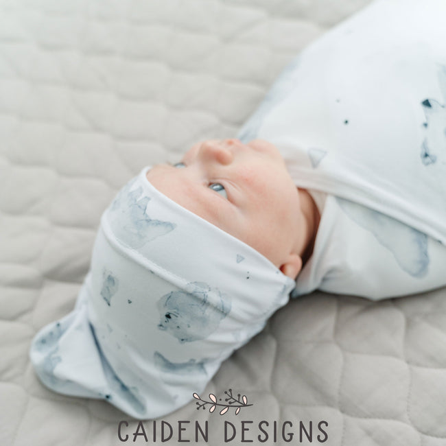 A baby wrapped in a monochrome watercolor polar bear swaddle blanket with a matching baby hat