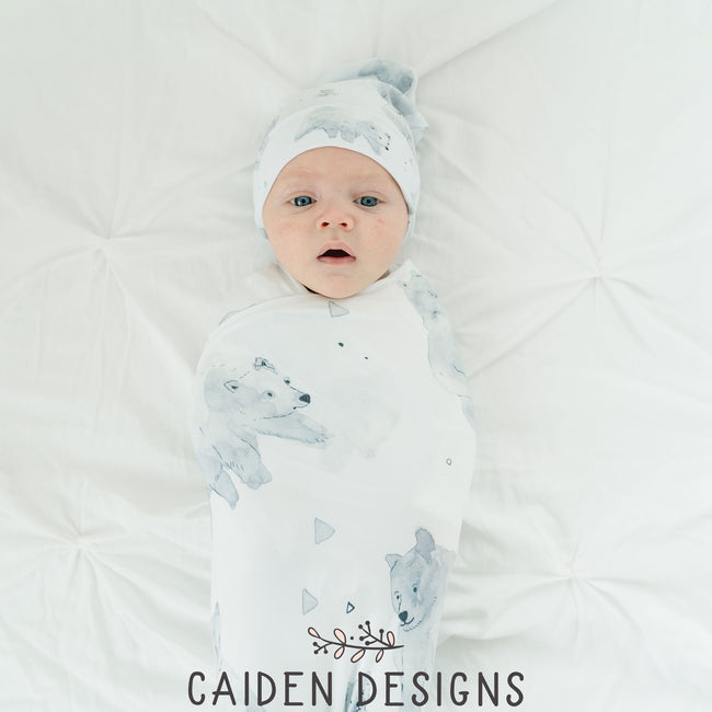 A baby wrapped in a monochrome watercolor polar bear swaddle blanket with a matching baby hat