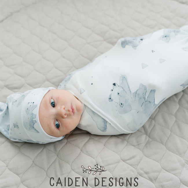 A baby wrapped in a monochrome watercolor polar bear swaddle blanket with a matching baby hat