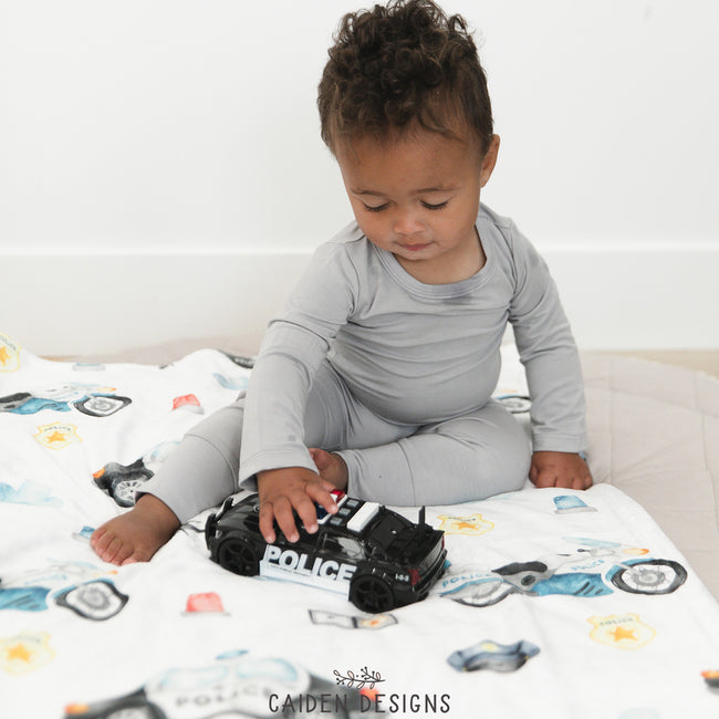 A baby sitting on a police-themed personalized baby blanket with various law enforcement vehicle toys