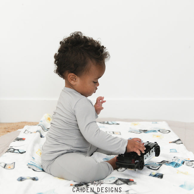 A baby sitting on a police-themed personalized baby blanket with various law enforcement vehicle toys