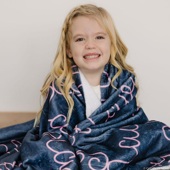 Little girl wrapped in a navy blue personalized blanket with pink name Navy