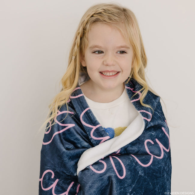 Little girl wrapped in a navy blue personalized blanket with pink name Navy