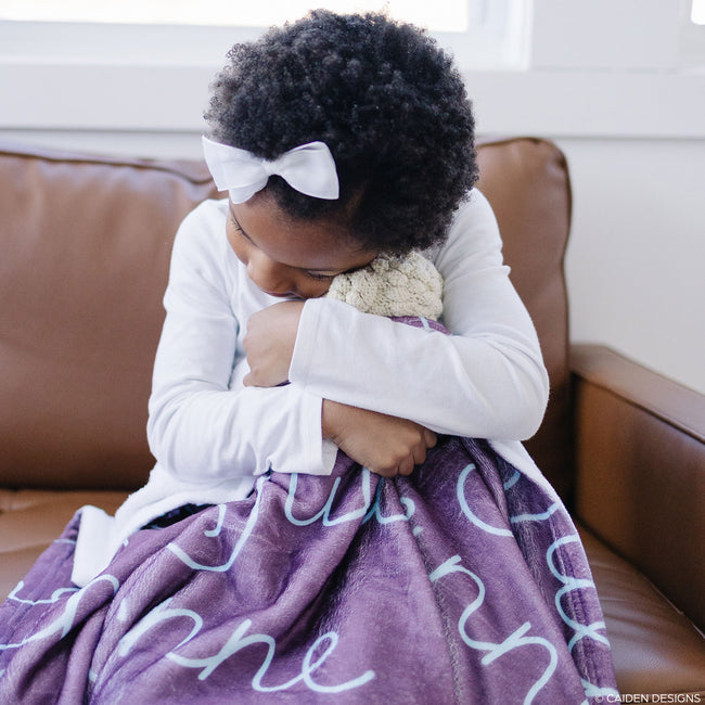 Little girl hugging a lamb stuffed animal and a plum personalized blanket on her lap