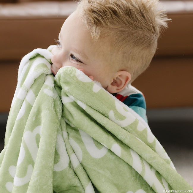 Little boy on the floor with a green personalized blanket with names on it