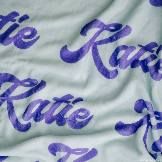 Close up of a soft pink personalized blanket with purple name "Katie" on it
