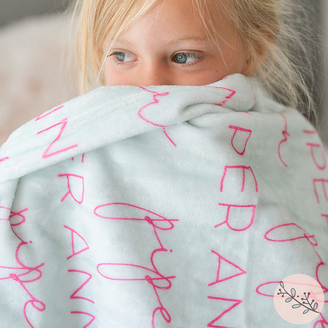 A young girl wrapped in a soft, plush blanket with personalized printed text on it.