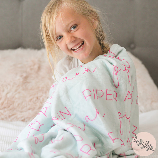 A young girl smiling and wrapped in a soft, plush blanket with personalized printed text on it.