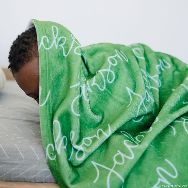 Young boy hiding under a green personalized blanket
