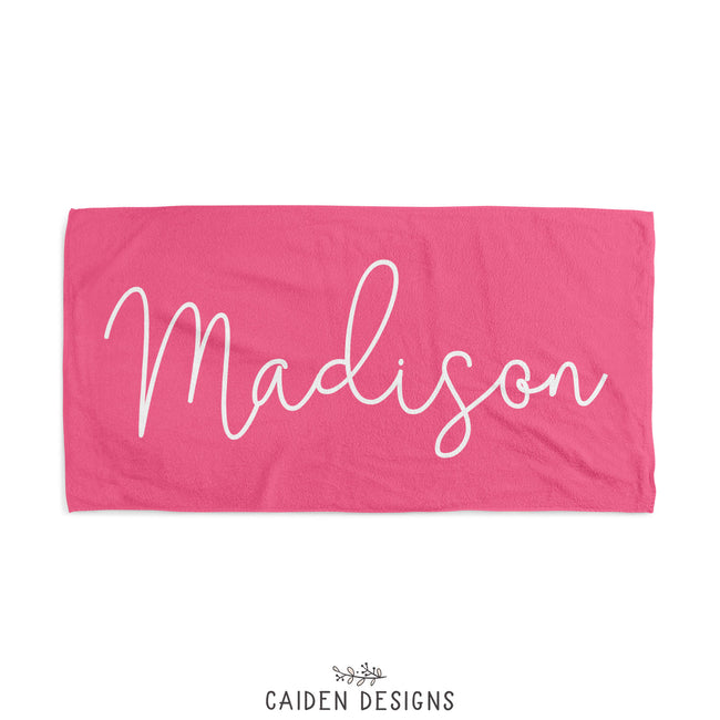 A pink personalized beach towel with the name 'Madison' printed in white on the front. The reverse side is solid white.