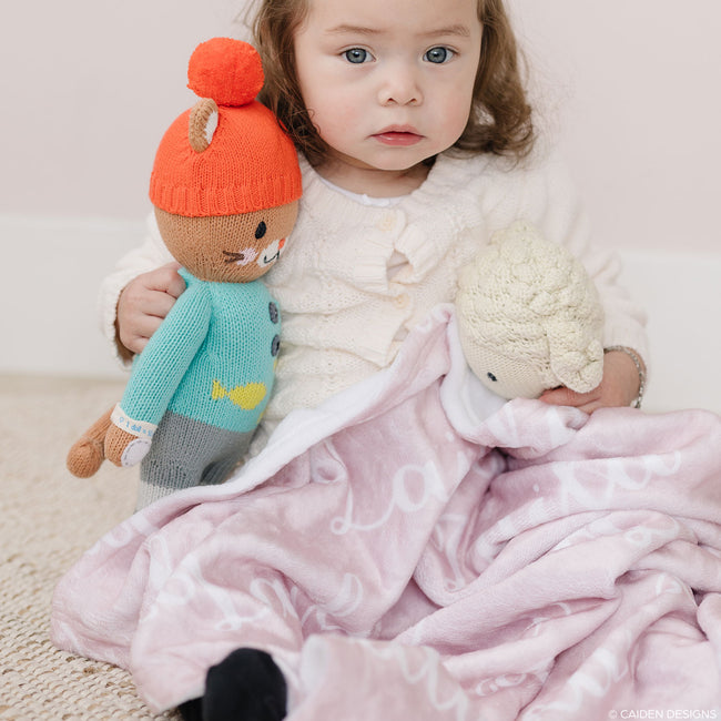 A little girl with stuffed animals and a soft pink personalized blanket