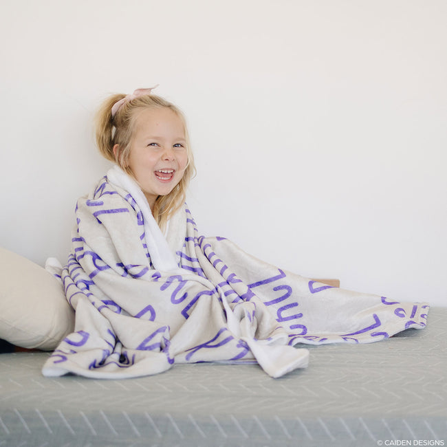 A little girl with a beige personalized blanket with name in purple
