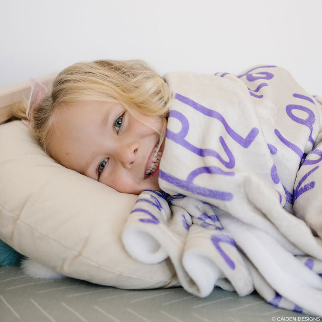 A little girl with a beige personalized blanket with name in purple