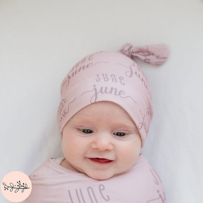a smiling baby girl wearing a pink personalized baby hat with the name June