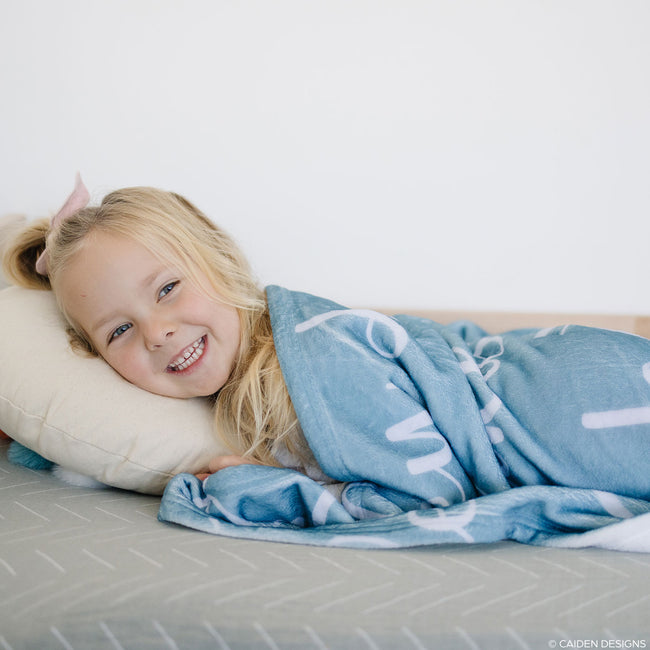 A little girl laughing with a blue personalized blanket with names on it