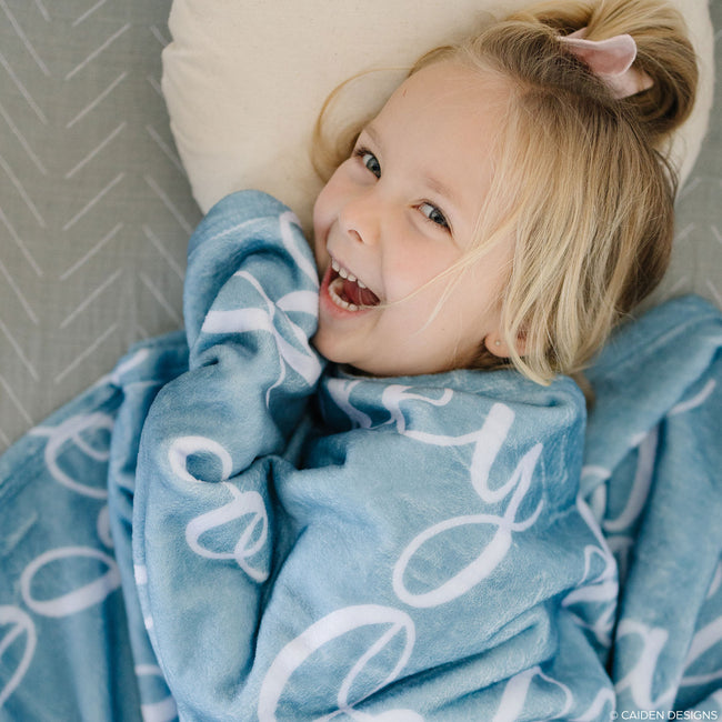 A little girl laughing with a blue personalized blanket with names on it