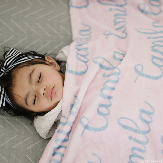 A little girl sleeping under a blue personalized name blanket