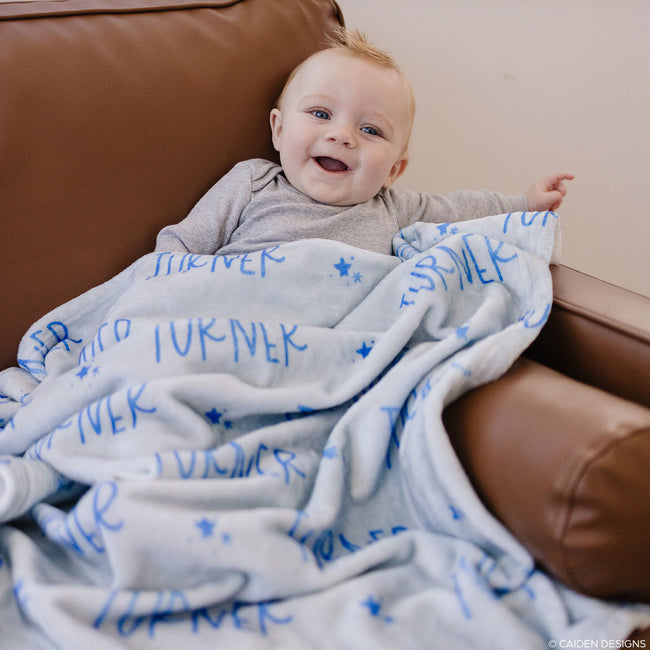 A little boy on a sofa with a light blue personalized blanket with names on it