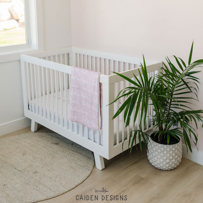 A personalized crib sheet with the name 'Lola Ann' printed in a cursive script on a crib and a matching personalized baby blanket