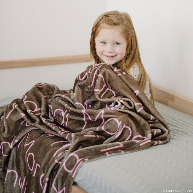 Little girl sitting on a bed with a brown personalized blanket with names on it