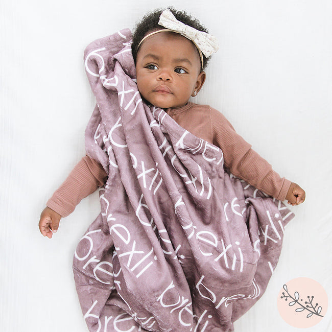 Baby girl with a mauve personalized baby blanket with names