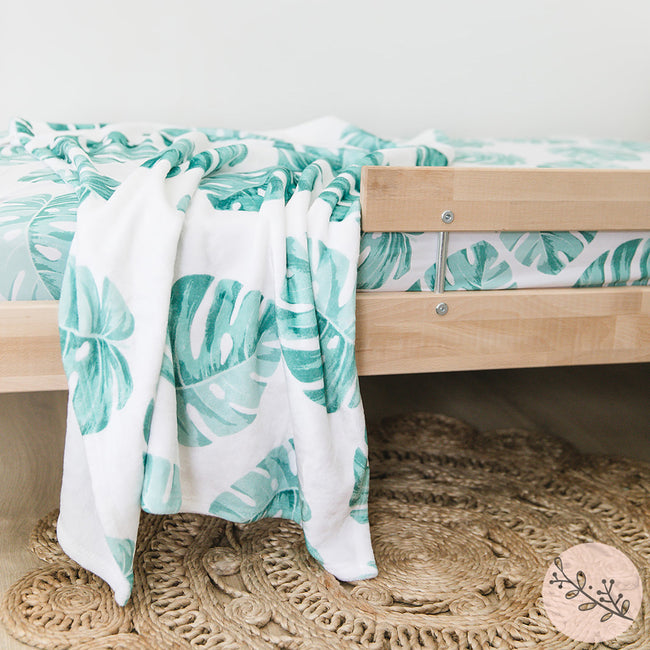 A tropical monstera leaves plush blanket on a bed with matching fitted sheet
