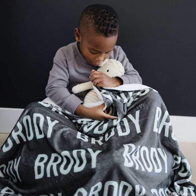 a little boy with a charcoal personalized blanket with the name Brody and a lamb stuffed animal