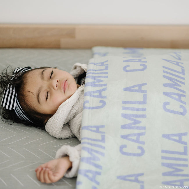 A girl sleeping covered by a soft mint personalized name blanket with the name Camila