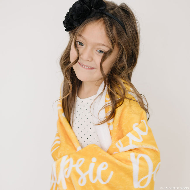 A child holding a yellow personalized blanket with printed names.