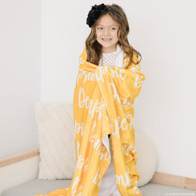 A child holding a yellow personalized blanket with printed names.