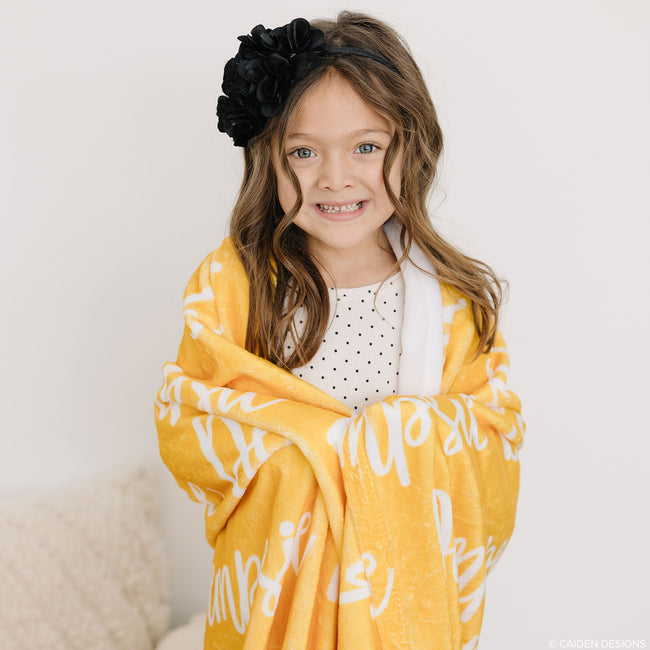 A child holding a yellow personalized blanket with printed names.