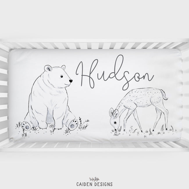 A personalized crib sheet with the name 'Hudson' printed on it, featuring a watercolor illustration of a bear and a deer.
