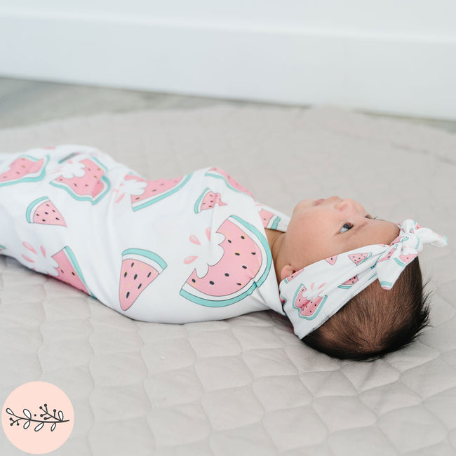 Baby wrapped in a pink watermelon pattern with a matching headband